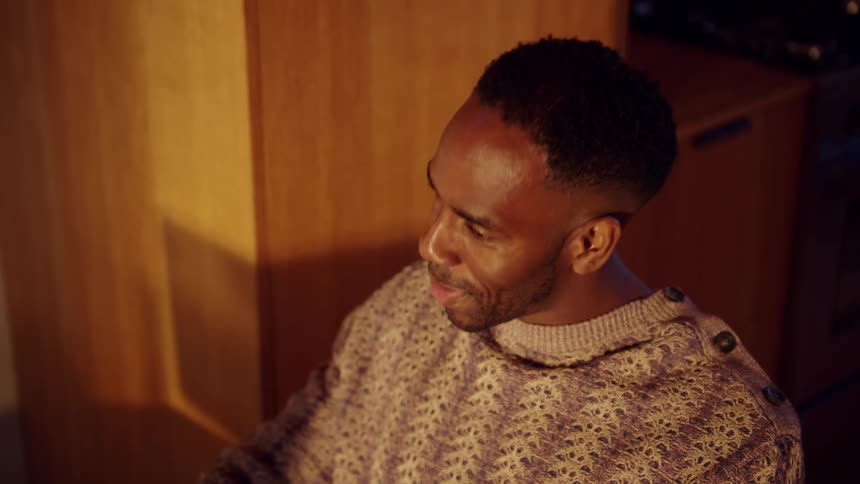 Man smiles while looking at a screen in an indoor setting with warm lighting