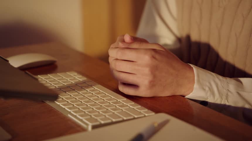 The man is sitting at the desk in front of his keyboard