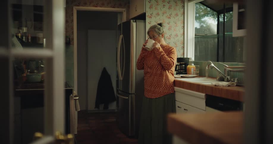 The woman drinks from her mug and leaves the room
