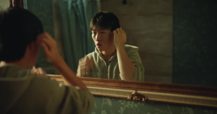 Person adjusts hair in front of a mirror in a bathroom with indoor lighting