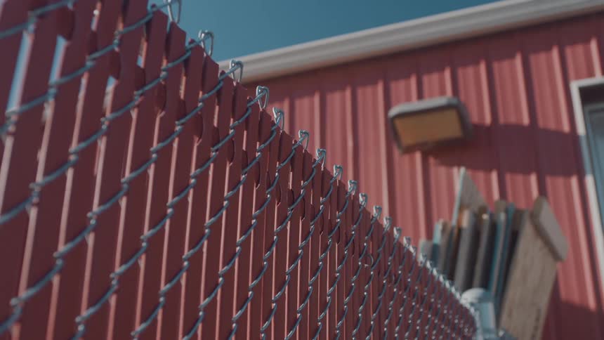 The wood leans on the fence by the warehouse