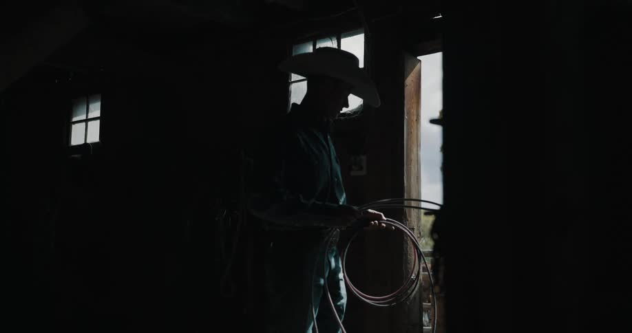 The cowboy lifts up his lasso in the barn