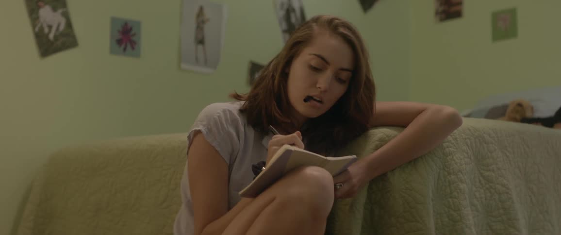 A woman writes in a notebook while sitting on a bedroom floor