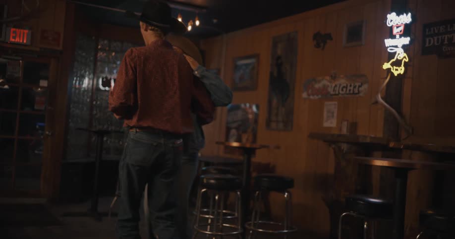 Couple dances together in a bar wearing cowboy hats under low lighting