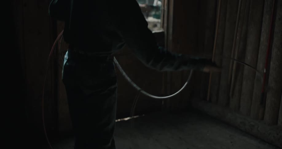Young adult man making rodeo moves with a rope indoors during day time