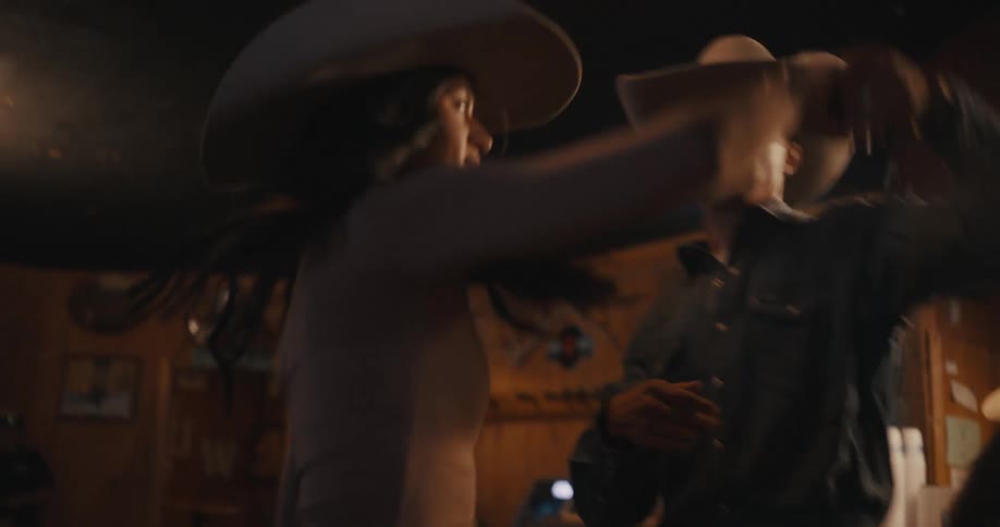 Couple dancing indoors wearing westernstyle outfits and hats under low lighting