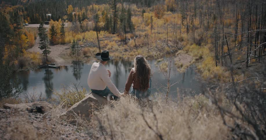 Couple sitting by a lakeside in a natural area surrounded by autumn vegetation