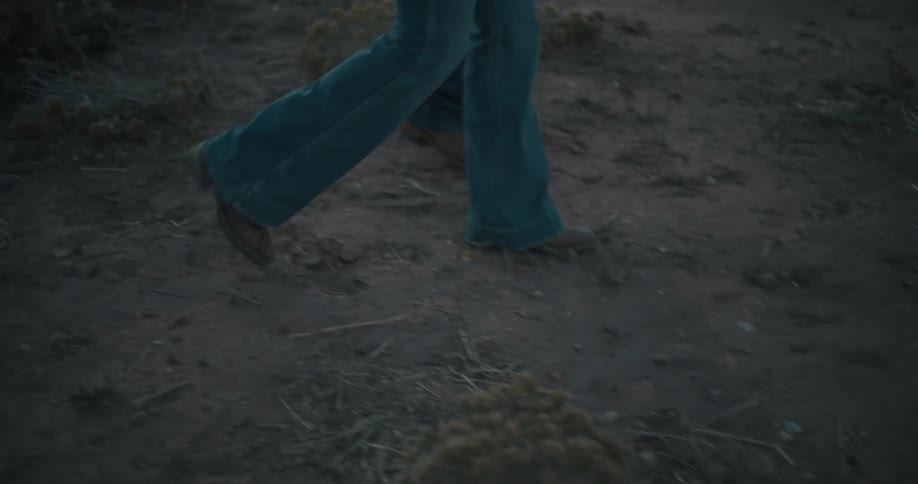 Booted steps on dirt ground in an outdoor setting with sparse vegetation