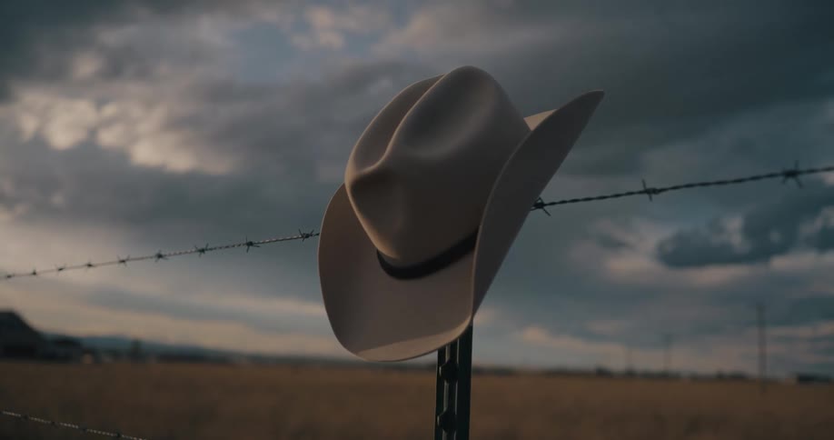 Cowboy hat hanging on a barbed wire fence in the country