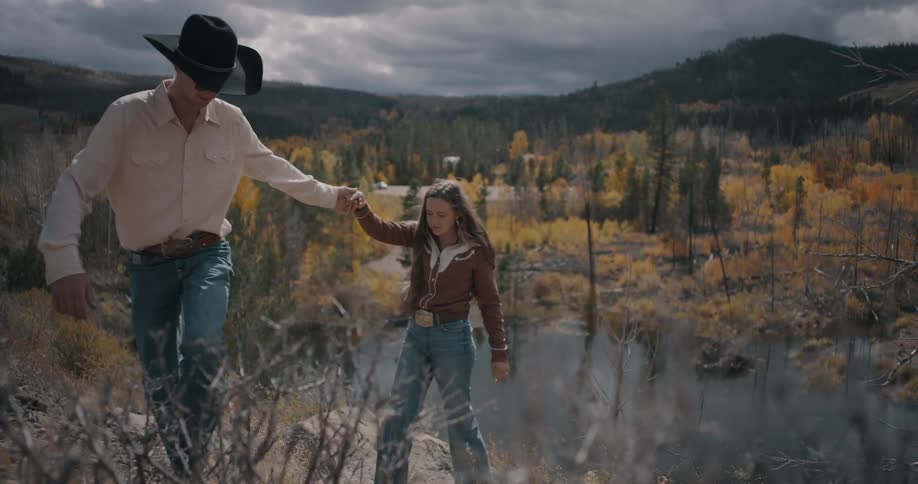 Man and a woman walk hand in hand along a trail near a river in an autumnal landscape