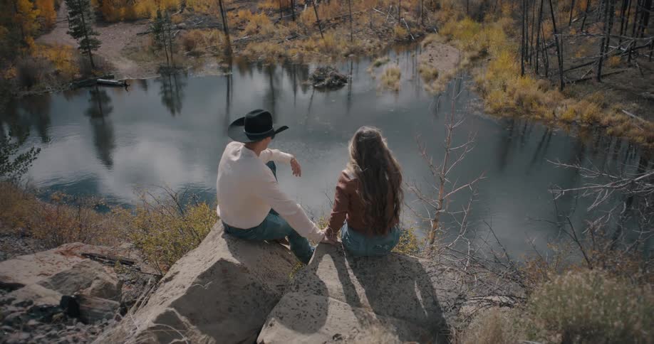 Couple sits on rocks overlooking a lake surrounded by trees in a natural landscape