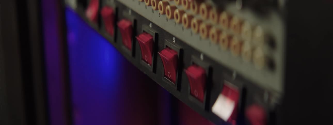 Finger presses a red switch on a control panel with rows of electrical connections