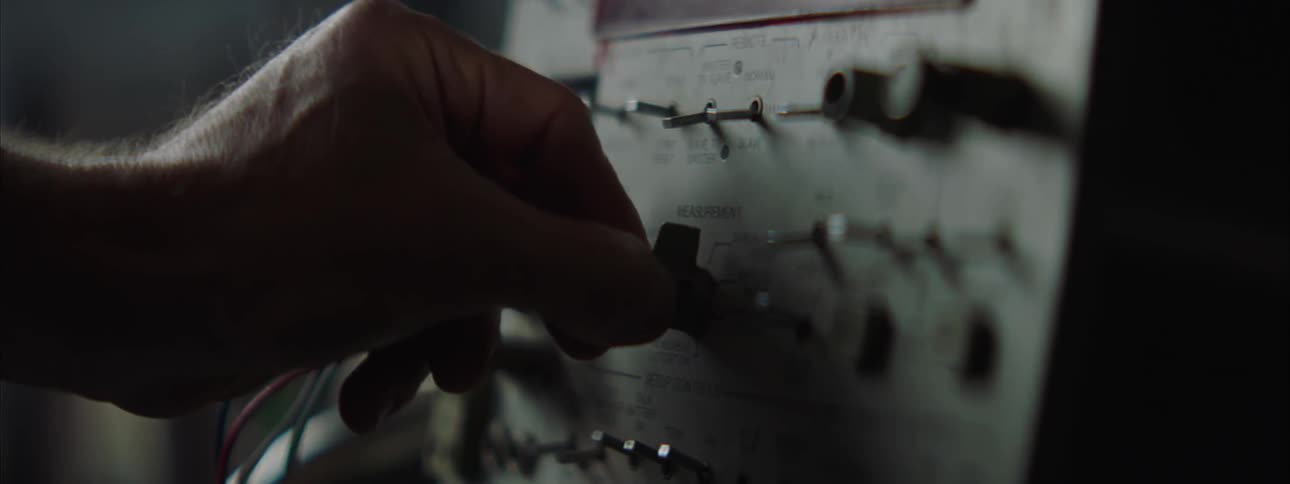 Hand adjusts a knob on an electronic panel with switches and metal connections