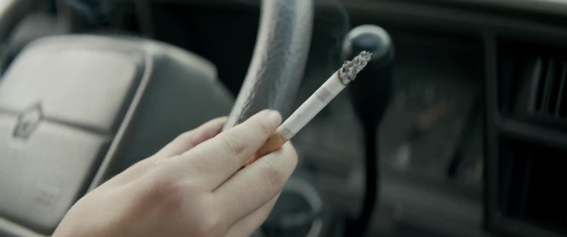 A person is sitting in a vehicle smoking a cigarette