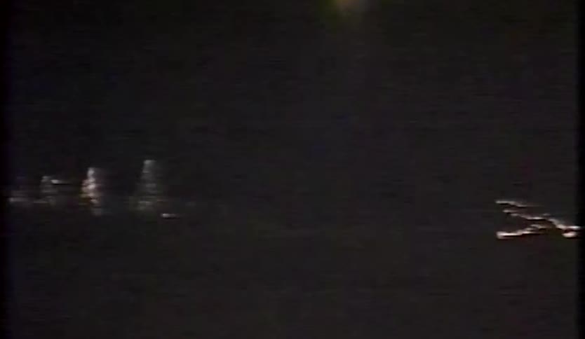 Distant city lights glow at night partially obscured by shadows in the foreground