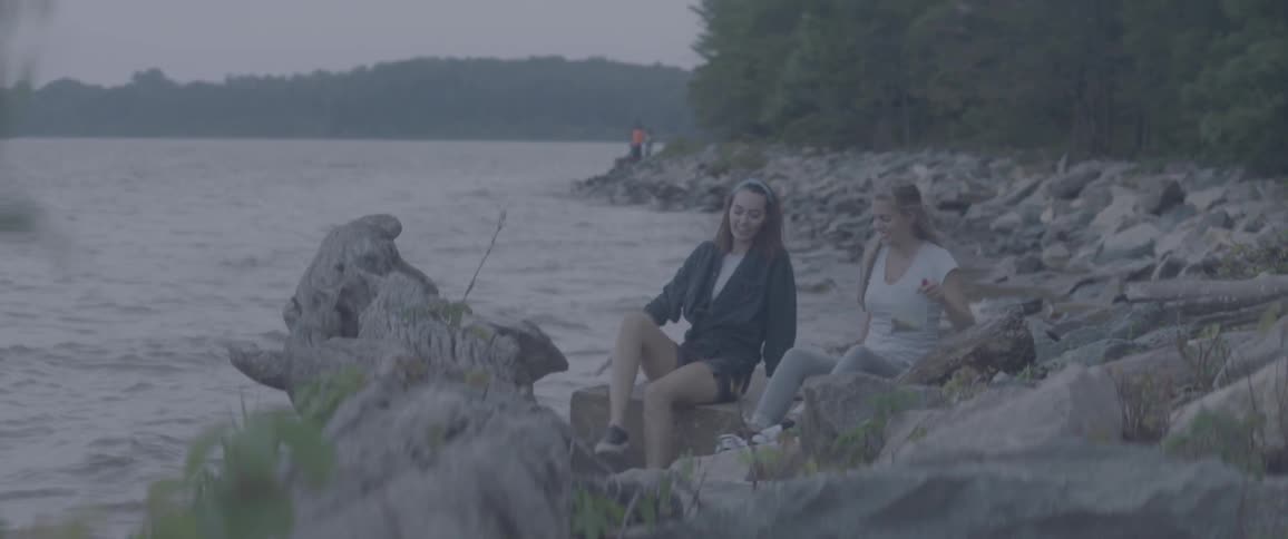 Two women sit on a rocky lakeshore