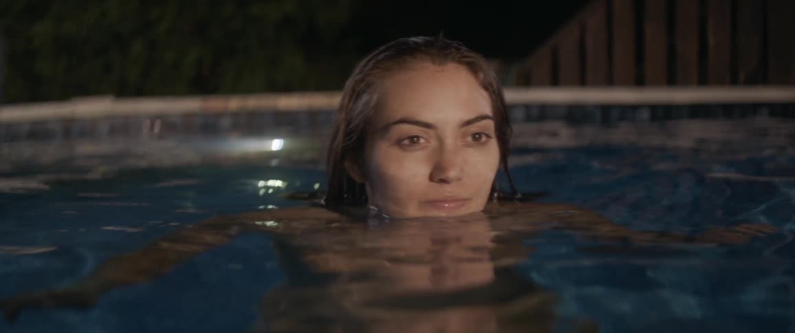 Woman dipping her face into water in pool at night