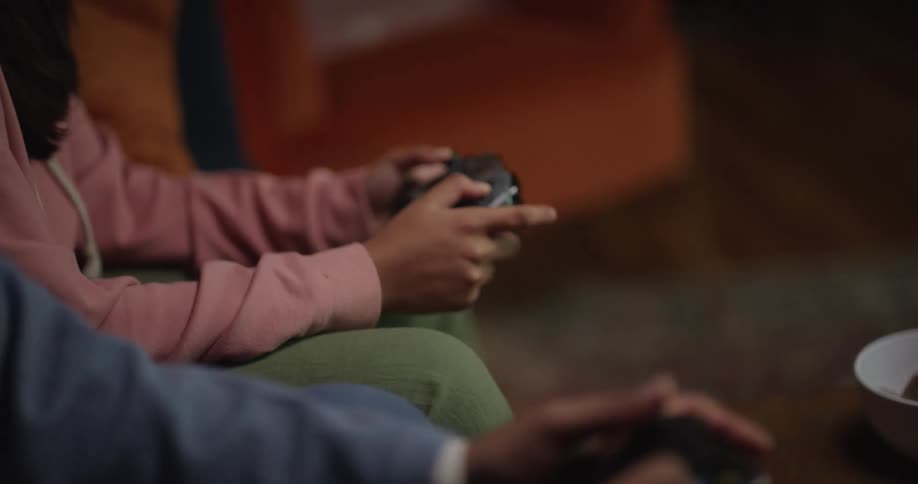 Two people are sitting playing video games with controllers in the living room