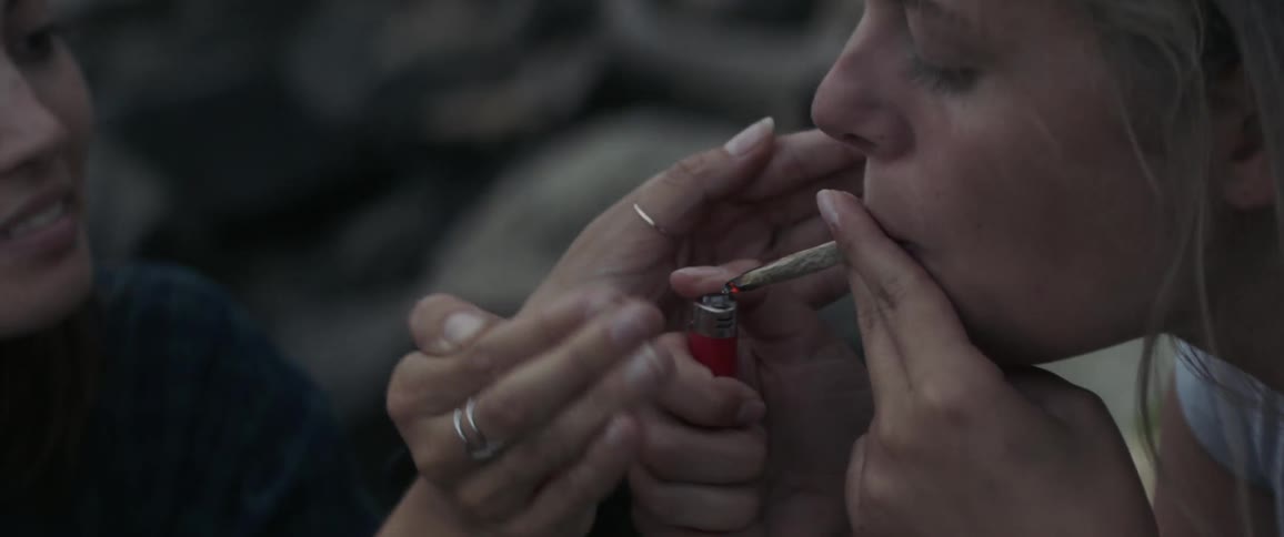 A woman helps another light a joint