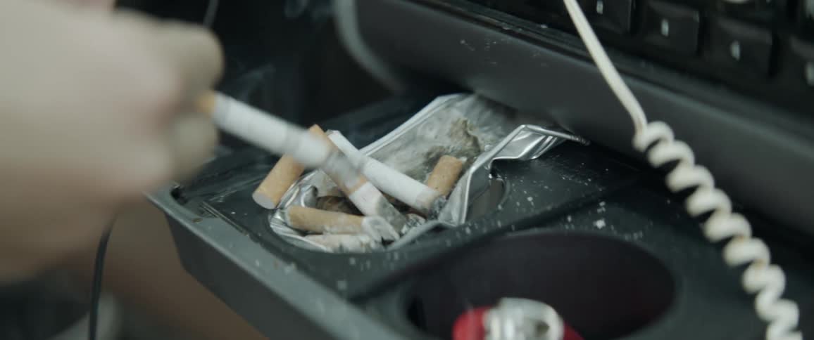 A person smokes a cigarette and flicks the ashes in an ashtray