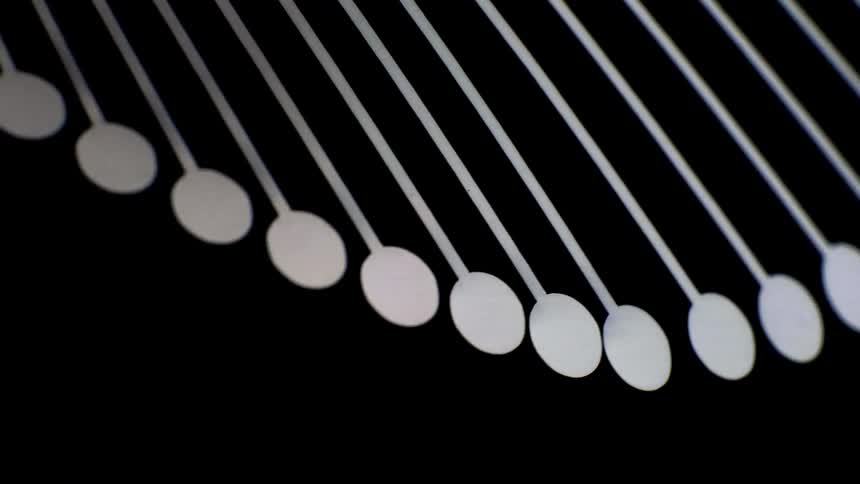 White circular pendulums on thin wires form a geometric pattern against black background