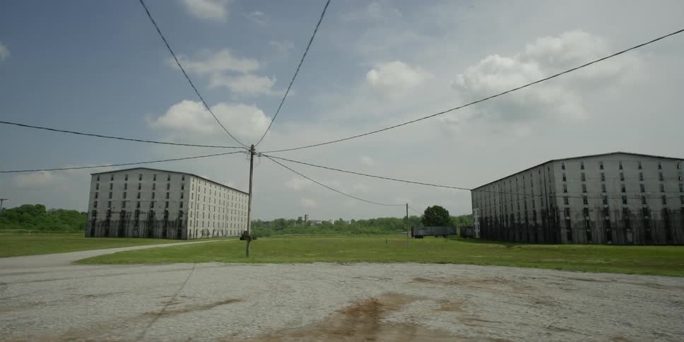 Two large buildings and cable wires on a flat grassy area with white clouds in the sky