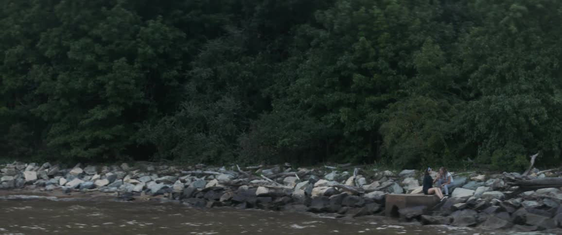 Two women sitting on rock next to rough body of water