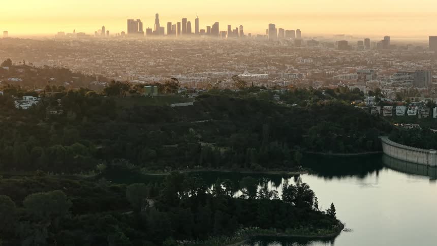 Reservoir surrounded by greenery with urban skyline at sunset