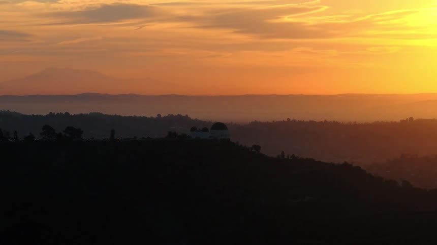Dark hills in foreground beneath golden sky with mountains in the distance