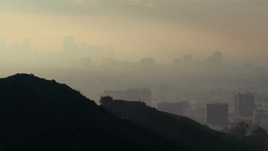 Silhouette of wooded hill facing city shrouded in haze at dusk