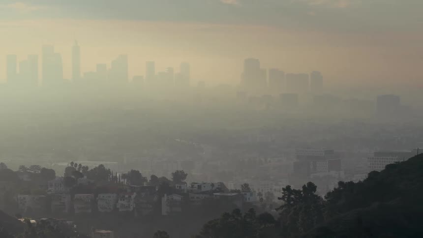 Metropolitan area surrounded by hills and covered in smog outdoors during dusk or dawn
