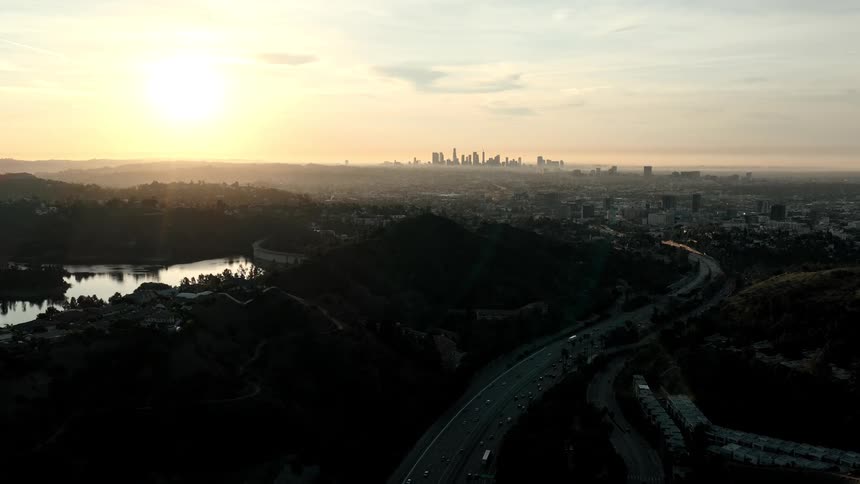 Winding highway through hills overlooking city at sunset