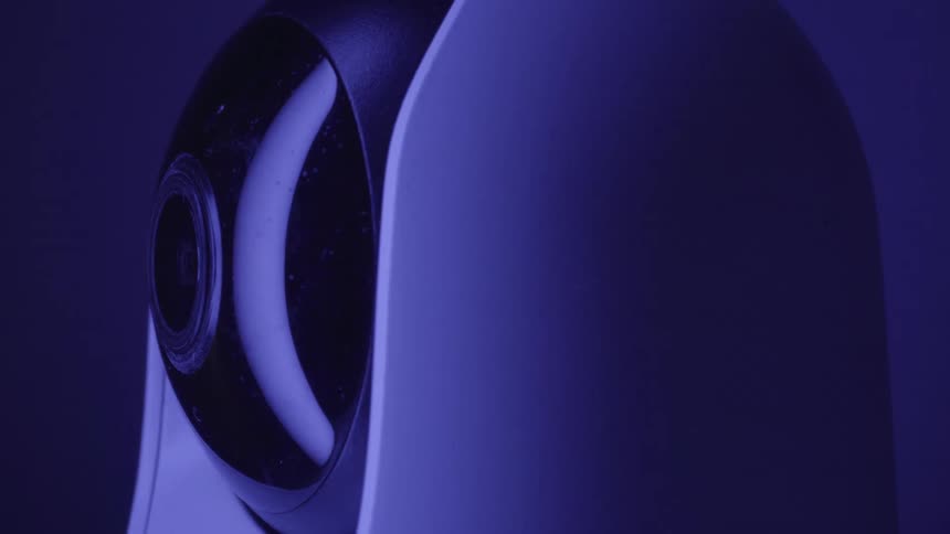 A cctv camera rotates in a full 360degree sweep inside a room illuminated by soft purple light