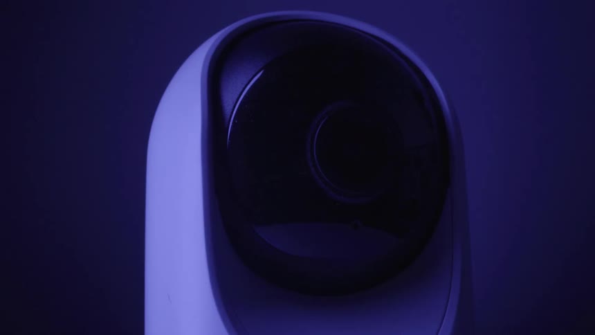 This video features a white domeshaped security camera with a black lens housing that slowly tilts upward and rotates away from the viewer the entire sequence is captured under a deep blue light giving the device a hightech and somewhat mysterious app