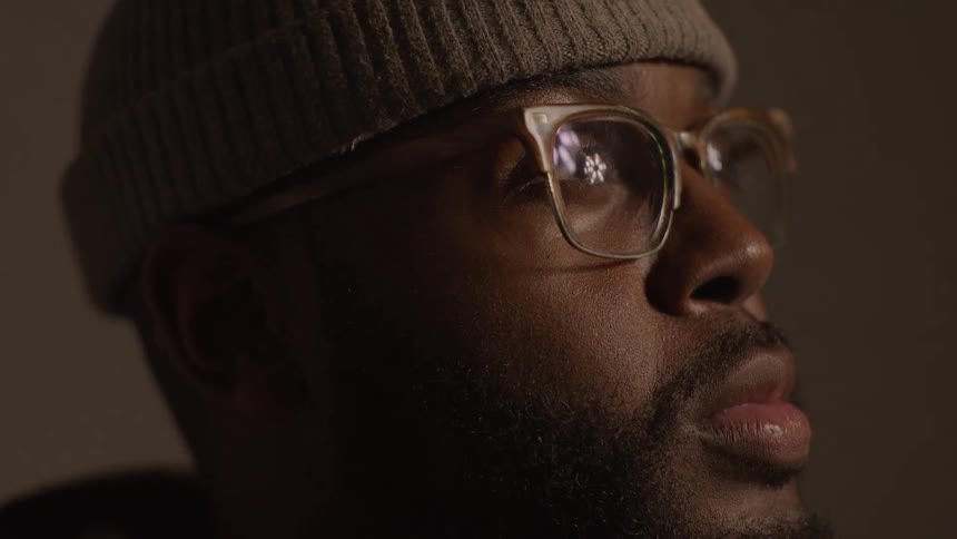 Closeup face of a black man with glasses and a cap with lights hovering over the face