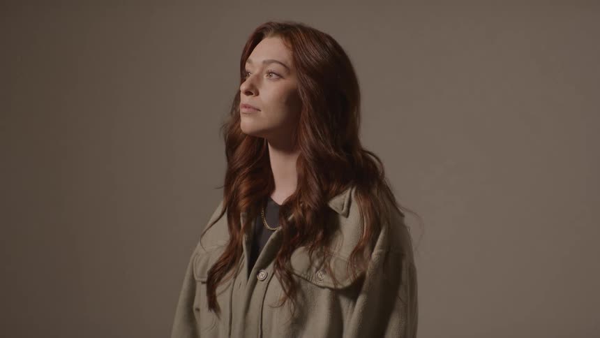 Woman with wavy hair wearing beige jacket against neutral background