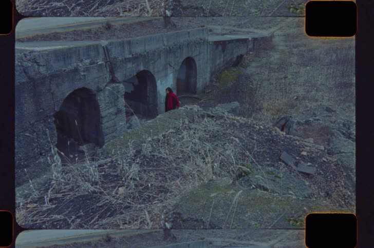 Person in red coat near concrete structure with arches in abandoned area