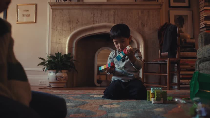 Little boy sits on the floor building with blocks as his little brother crawls around on the floor