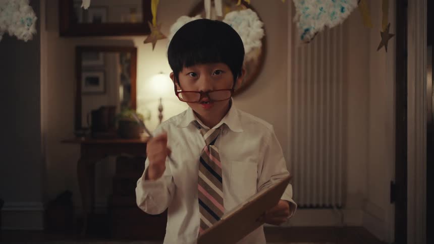 Boy with glasses in white shirt and striped tie holding clipboard in decorated setting