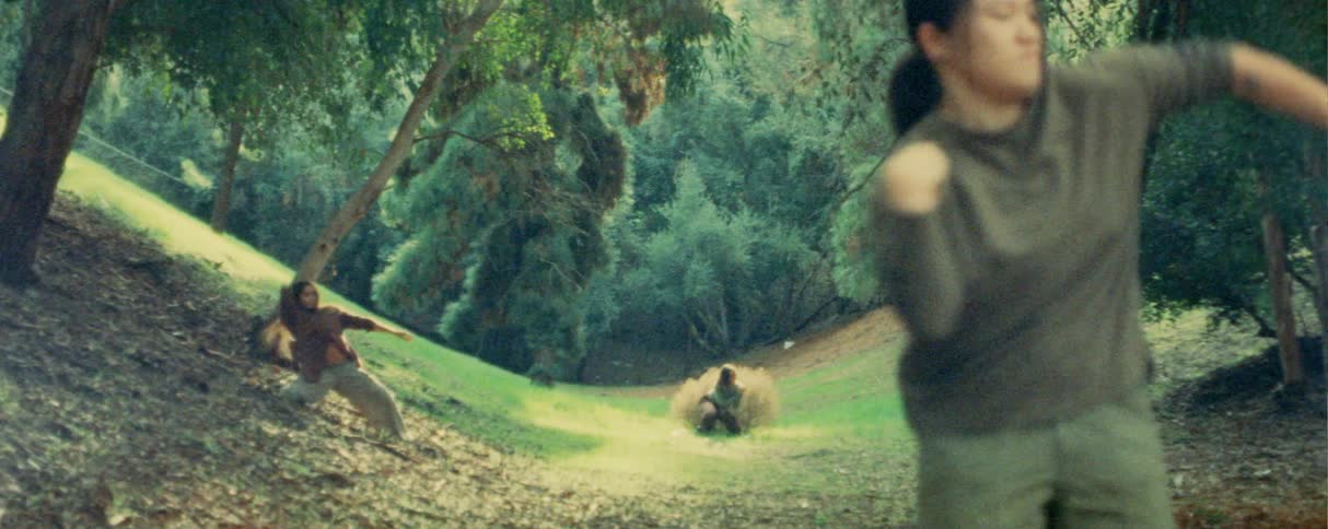 Three women stand along a path leading into the woods at midday each dancing in a different style