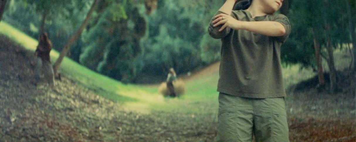 Person performs dance movements on a wooded path during daylight