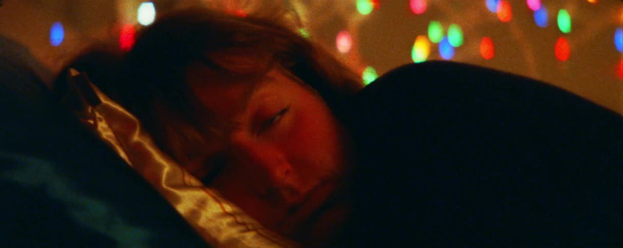A person lies with their head on a silk pillow while looking directly toward the camera in the background colorful outoffocus lights create a soft bokeh effect behind them