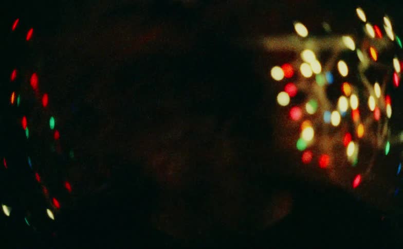 A young woman stands in a bedroom filled with colorful disco lights and glowing christmas lights her expression tense and her movements sharp as she reacts with visible anger