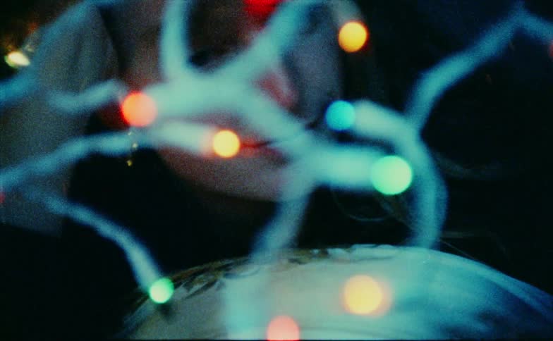 The woman smiles while touching a string of christmas lights