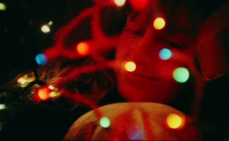 The string of christmas lights dangle in front of the womans face