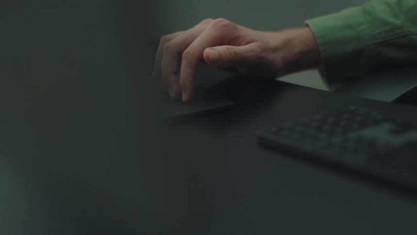 Man sitting at a table with a keyboard and his hand moving on a touch pad