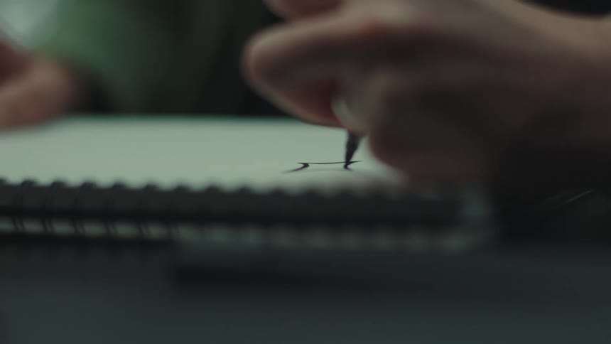 Close up of a person drawing a symbol on a page in a notebook placed on a table