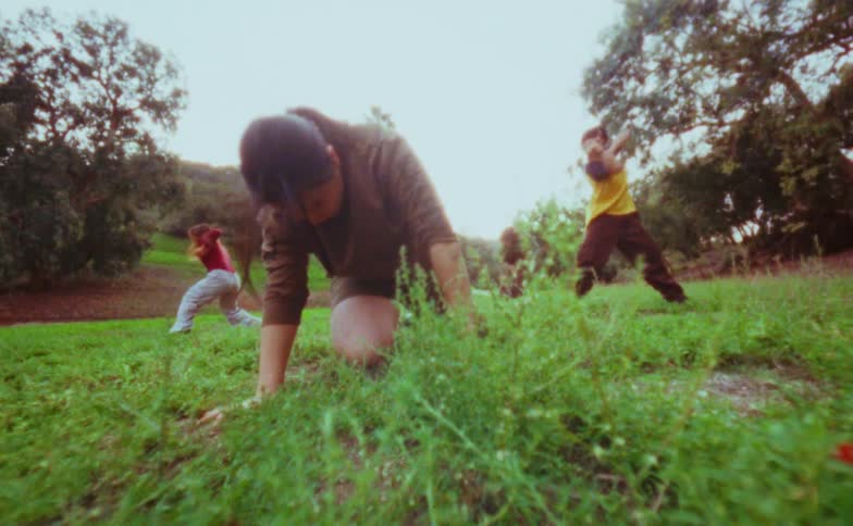 The woman is kneeling in the grass as others do tai chi