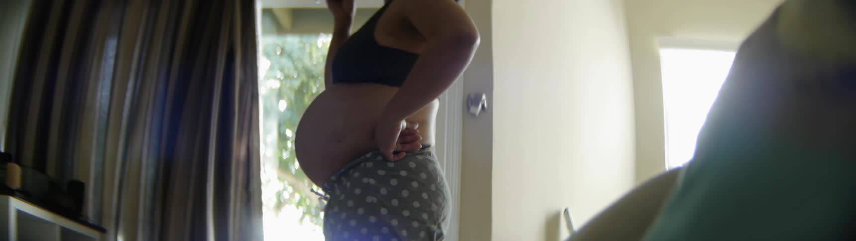 A pregnant woman wearing a sports bra drinks from a glass