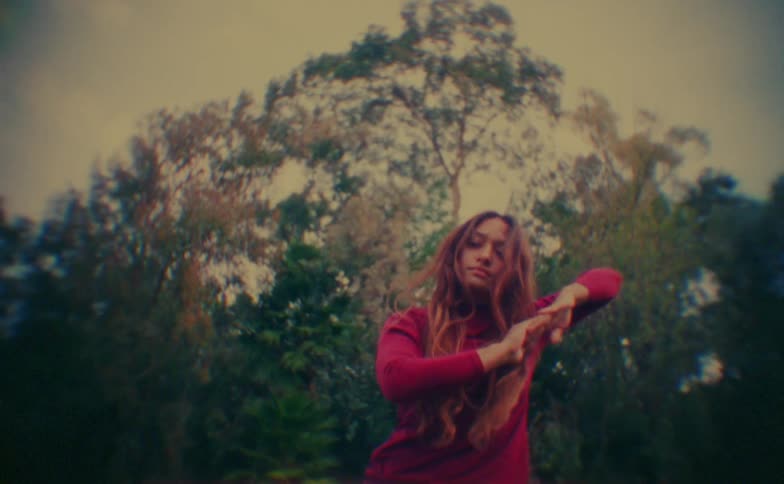 Person performs dance movements with arms in motion in an outdoor wooded setting